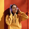 A young woman wearing purple headphones with cat ears and a yellow hoodie, smiling and touching her headphones, against a vibrant orange and yellow background. Náhľad obrázku produktu