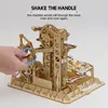 A hand is shown shaking the handle of a wooden marble run toy, with text explaining its function. Voir les images du produit
