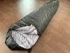 A black sleeping bag is laid out on a wooden floor, partially unzipped to reveal its gray interior. Produktbild-Vorschau