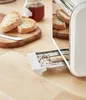 A toaster with a crumb tray pulled out, next to sliced bread and a jar of jam on a wooden surface. Podgląd zdjęcia produktu