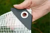 A hand holding a corner of a transparent tarp with a reinforced grommet. Anteprima dell’immagine prodotto
