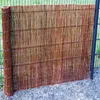 A rolled-up reed fence is placed against a metal fence in an outdoor setting. Produktbild-Vorschau