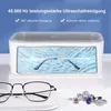An ultrasonic cleaner with glasses inside, and another pair of glasses and rings displayed in front. Produktbild-Vorschau