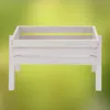 A white wooden planter box with legs is shown against a blurred green and yellow background. Produktbild-Vorschau