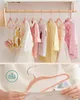 A split image showing children's clothing on hangers on a rack in the top half, and a close-up of a pink hanger being held by a person in the bottom half. Náhled obrázku produktu