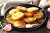 A close-up shot of roasted potatoes in a frying pan, garnished with rosemary and served with garlic cloves. Voir les images du produit