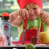 A child is holding two Opinel knives, one red and one green, over a plate with a small cake, an apple, and a lime. Produktbild-Vorschau