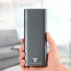 A hand holding a gray power bank with a logo on it, with a blurred background of a living room. Produktbild-Vorschau