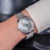 A close-up shot of a woman's wrist wearing a silver Guess watch with a mesh band and a crystal-embellished bezel. The watch face has a patterned silver dial. Náhled obrázku produktu