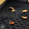 A close-up of a black car floor mat with water and fallen leaves on it. Produktbild-Vorschau