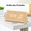 A wooden digital alarm clock displaying time, humidity, and temperature, placed on a marble-like surface with a plant and lamp in the background. Dimensions are indicated with text overlays. Produktbild-Vorschau