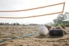 A volleyball, a JBL speaker, and a duffel bag are on a sandy beach next to a volleyball net. Náhľad obrázku produktu