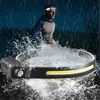 A person is running in the rain while wearing a headlamp. The headlamp is shown in the foreground, submerged in water. Náhled obrázku produktu
