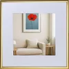 A framed picture of a red poppy on a wall above a sofa, with a small table and plant next to the sofa. Produktbild-Vorschau