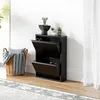 A black shoe cabinet with two open flip-down doors, placed on a wooden floor next to a woven basket with blankets and pillows. Produktbild-Vorschau