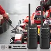 Two walkie-talkies are shown in the foreground with a go-kart track and racing helmets in the background. A hand is holding a charging cable in the left side of the image. Produktbild-Vorschau