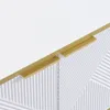 A close-up view of a white cabinet with gold handles and a geometric 3D front. Náhľad obrázku produktu