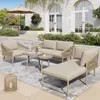 An outdoor patio scene with a 5-piece garden lounge set, including a sofa, armchair, chaise lounge, and two coffee tables, arranged on a rug. An umbrella is visible in the background. Podgląd zdjęcia produktu