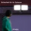 A person walks past a wall-mounted outdoor light fixture at night. Produktbild-Vorschau