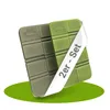 Two foldable seat cushions are shown, one green and one gray, with a white band across the green one that has text on it. The cushions are resting on a green oval shape against a white background. Produktbild-Vorschau