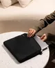 A person is placing a laptop into a black laptop sleeve on a round table. Produktbild-Vorschau