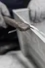 A close-up of hands wearing gloves using a tool to shape or trim a white object. Produktbild-Vorschau