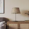 A wicker lampshade sits on a wooden cabinet next to a sofa and a framed picture. Produktbild-Vorschau