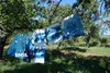 Several pieces of fabric dyed with a blue tie-dye pattern are hanging on a clothesline in an outdoor setting, with trees and a cornfield in the background. Produktbild-Vorschau