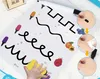 A child's hand is shown erasing markings from a dry-erase learning board with various tracing lines and colorful illustrations of fruit and markers. Insets demonstrate how to clean the board. Podgląd zdjęcia produktu