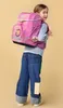 A young girl wearing a pink backpack and jeans, looking over her shoulder. Voir les images du produit