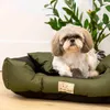 A small dog is resting in a green dog bed next to a potted plant. Náhled obrázku produktu