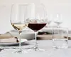 Two wine glasses, one with white wine and one with red wine, are set on a table with other glassware and a plate with food. Náhľad obrázku produktu