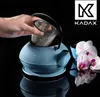 A hand is placing a tea strainer into a blue teapot, with orchids and a cup in the background. Náhled obrázku produktu