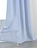 A light blue curtain is draped over a small table with a teacup and saucer. Produktbild-Vorschau
