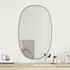 A black oval mirror is mounted on a white wall above a wooden dresser. The dresser is decorated with various cosmetic items and a small framed picture. Podgląd zdjęcia produktu
