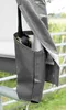 A close-up view of a gray tarp material with a metal pole and a strap with a buckle. The background shows a fence and greenery. Produktbild-Vorschau