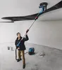 A man is using a long-handled sander on a ceiling in an unfinished room, with a vacuum cleaner nearby. Podgląd zdjęcia produktu