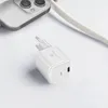 A white GaN 65W USB-C power adapter is shown on a white surface next to a portion of a smartphone. Náhled obrázku produktu