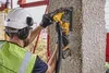 A construction worker is using a DeWALT Akku-Mauernutfräse to cut into a concrete pillar. Voir les images du produit