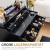 A black vanity table with multiple drawers filled with cosmetics, set in a bedroom environment. Produktbild-Vorschau