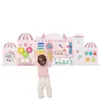A child is interacting with a large, pink, castle-themed activity wall designed for toddlers. Produktbild-Vorschau