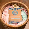 A package of OceanWash laundry detergent sheets is placed in a woven basket filled with clean laundry. Produktbild-Vorschau