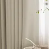 A close-up view of a beige fabric curtain with vertical pleats, showing texture and stitching detail. A small green plant branch is visible to the right, and a gift box with ribbon is in the foreground. Produktbild-Vorschau