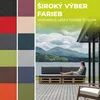 A woman is sitting on a sofa made of pallets by a lake, with a view of mountains. Náhľad obrázku produktu