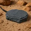 A close-up of a rock-shaped heating device on a sandy surface with other rocks in the background. Anteprima dell’immagine prodotto