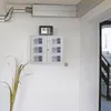 A wall-mounted storage unit with multiple small safes, a small safe on top, and some plant leaves in the foreground. Produktbild-Vorschau