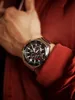 A close-up shot of a person's wrist wearing a silver and black watch with red accents. Voir les images du produit