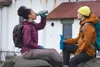 Two people sitting on rocks, drinking from water bottles. Produktbild-Vorschau