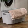 A laundry basket filled with towels sits on a wooden floor next to a washing machine. Produktbild-Vorschau