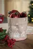 Christmas ornaments in a decorative fabric bin on a wooden table, with festive greenery and berries in the foreground. Anteprima dell’immagine prodotto